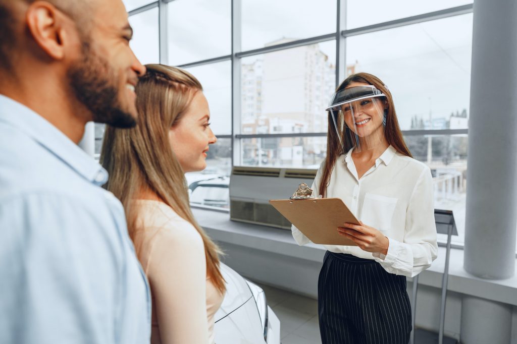 Woman car dealer consulting buyers wearing medical face shield