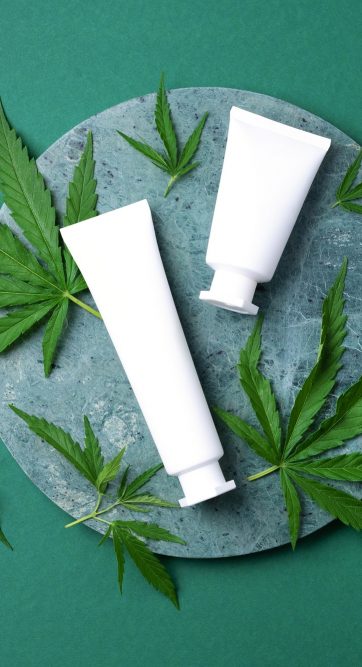 Cosmetic product with CBD oil and hemp leaves on marble background. Flat lay, copy space. Top view